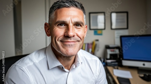 A cheerful man sits confidently at his desk, engaged with a computer and advanced office tools, surrounded by a clean, bright workspace