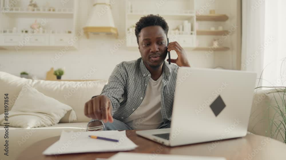 Home office of freelancer, African American man calling by phone, using laptop. Freelance and startup, employee working remotely, busy and multitasking person, distant communication with partners Home office of freelancer, African American man calling by phone, using laptop. Freelance and startup, employee working remotely, busy and multitasking person, distant communication with partners