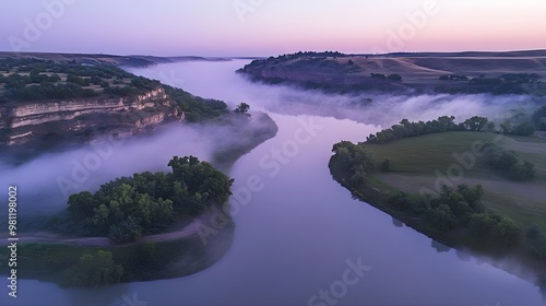 Serene landscape featuring a misty river winding through lush green hills at dawn, creating a tranquil and peaceful atmosphere.