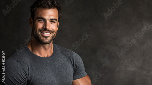 Smiling man in a grey t-shirt strikes a pose against a dark grey backdrop