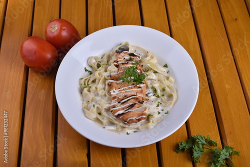 Fettuccine Alfredo with chicken served in a bowl, captured from an angle view. The creamy sauce and pasta create an appealing presentation for a restaurant setting. photo