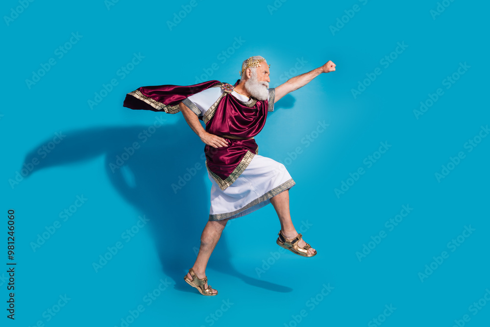 Obraz premium Full size photo of powerful mature man raise fist flying running wear ancient roman emperor tunic isolated on blue color background