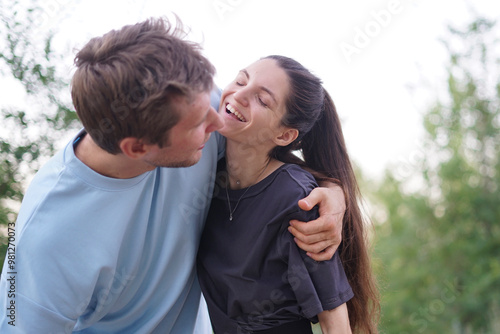 A man and woman are hugging in a park, smiling at each other. They are happy and playful