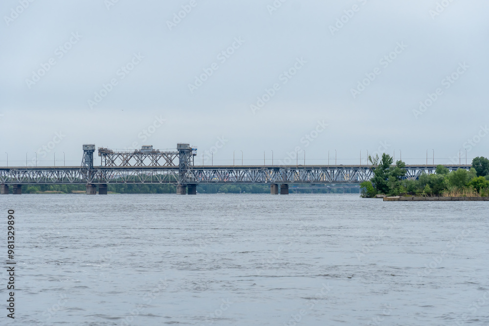 View on road and railway bridge through river. Panorama on bridge for train cargo and passenger transport. Architectural structure connecting left and right banks city. Infrastructure Dnipro Ukraine. View on road and railway bridge through river. Panorama on bridge for train cargo and passenger transport. Architectural structure connecting left and right banks city. Infrastructure Dnipro Ukraine.