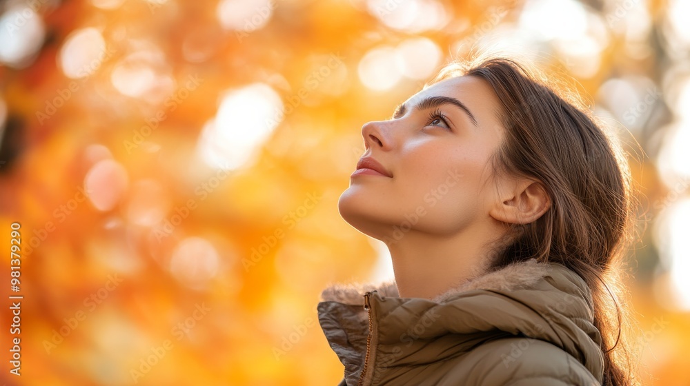 A woman wearing a warm jacket looks up with a thoughtful expression, surrounded by the warm, golden light of autumn leaves glowing in the background A woman wearing a warm jacket looks up with a thoughtful expression, surrounded by the warm, golden light of autumn leaves glowing in the background
