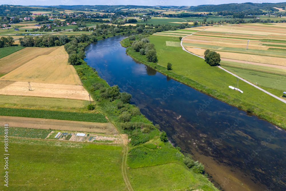 Naklejka premium Aerial view of a tranquil river winding through vibrant green fields and farmland, showcasing the beauty of the rural landscape.