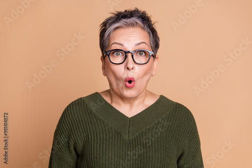 Photo of speechless woman with short hairdo dressed khaki knit sweater in glasses astonished staring isolated on beige color background