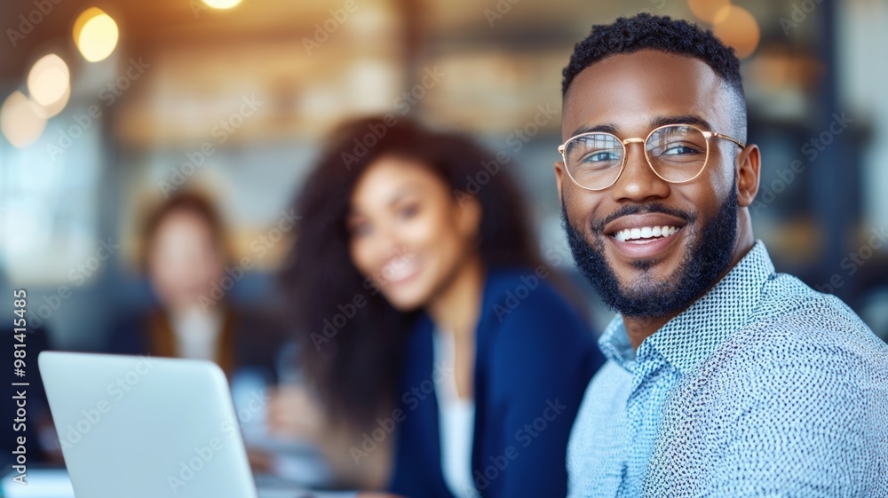 A man with glasses is smiling and sitting in front of a laptop A man with glasses is smiling and sitting in front of a laptop