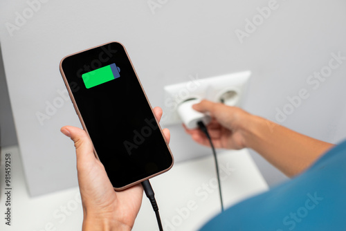 Lady holding cellphone while putting on charging into wall outlet. Charging phone with regular charger concept photo