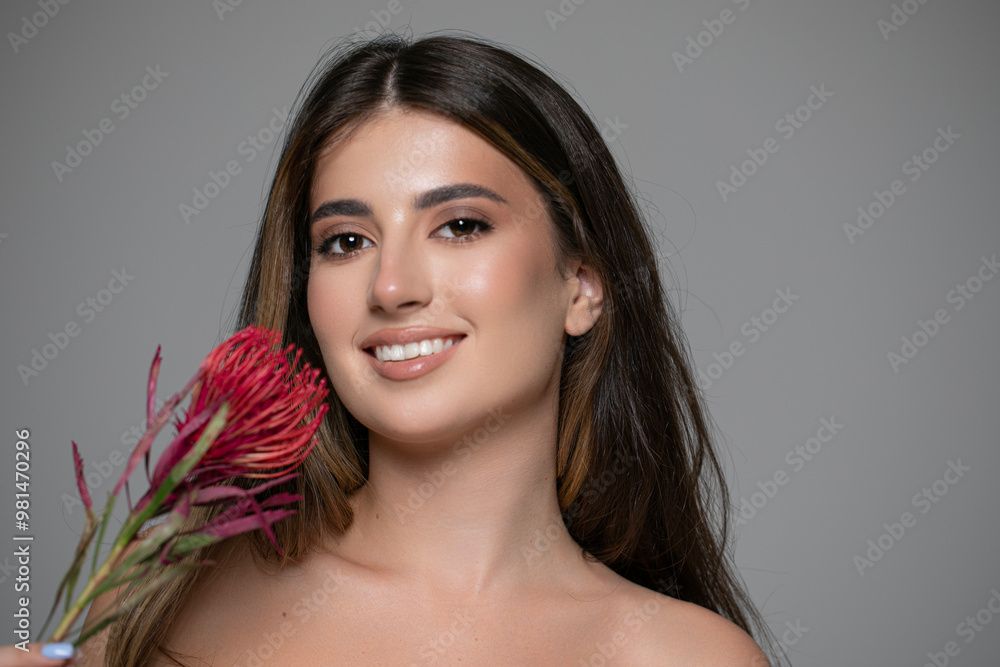 Front portrait of a beautiful smiling young woman in a black dress with bare shoulders, posing in studio with a pink flowers. Front portrait of a beautiful smiling young woman in a black dress with bare shoulders, posing in studio with a pink flowers.