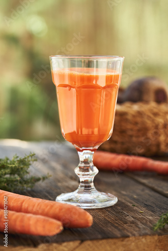 A glass of fresh carrot juice on a wooden table outdoors