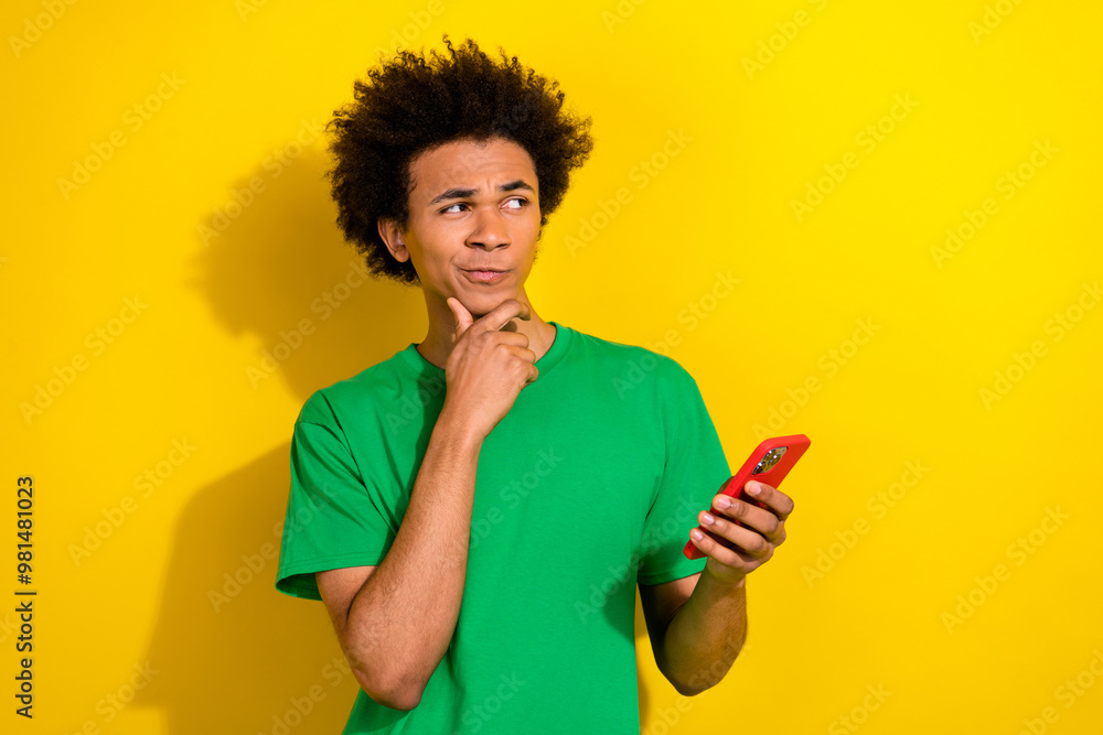 Photo of doubtful unsure guy dressed green t-shirt tyhping modern gadget looking emtpy space isolated yellow color background Photo of doubtful unsure guy dressed green t-shirt tyhping modern gadget looking emtpy space isolated yellow color background