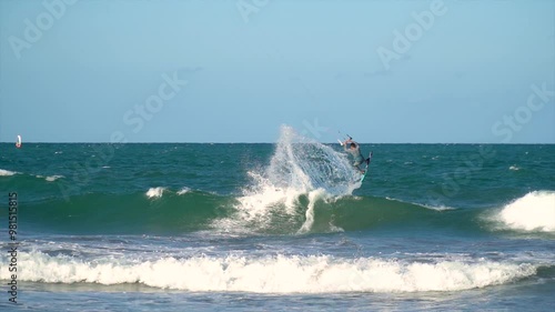Slow motion, young sporty man kitesurfing in the sea at sunset.