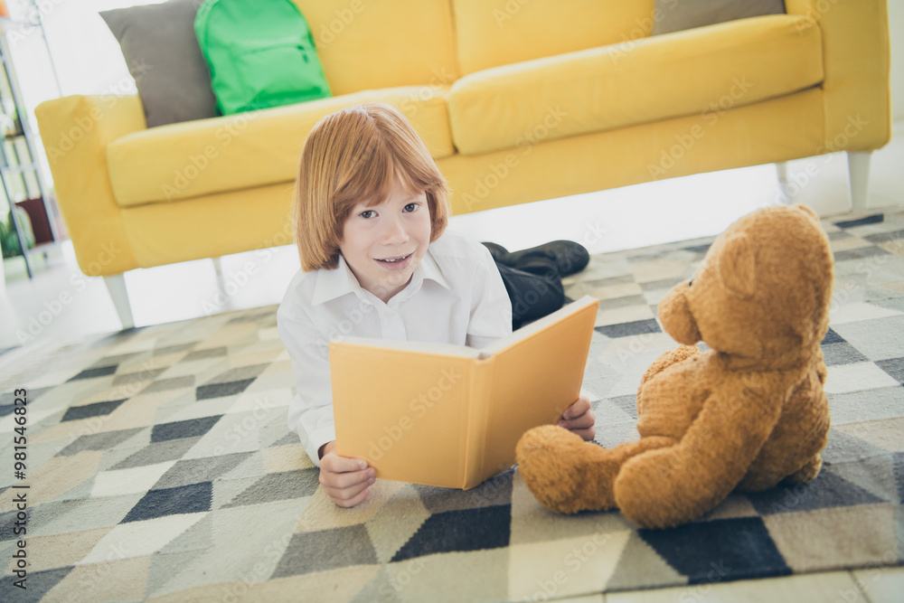 Fototapeta premium Photo of cute adorable funny cheerful small boy lying carpet cozy room daylight indoors reading story