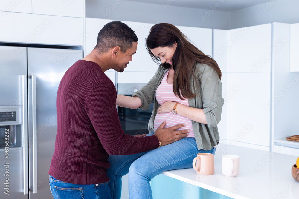 At home, expectant multiracial couple in kitchen, man touching woman's pregnant belly, smiling At home, expectant multiracial couple in kitchen, man touching woman's pregnant belly, smiling