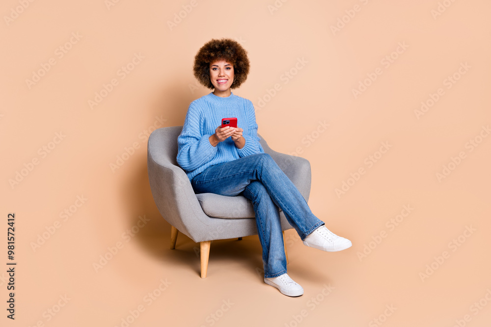 Full size photo of smart girl dressed knit sweater sit on armchair holding smartphone in hands isolated on pastel color background Full size photo of smart girl dressed knit sweater sit on armchair holding smartphone in hands isolated on pastel color background