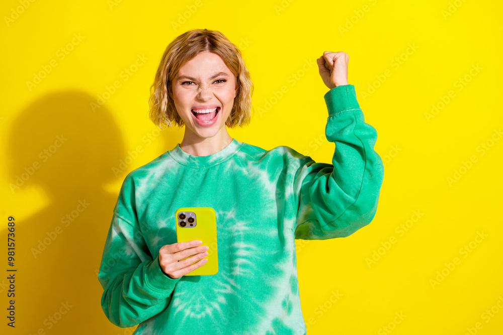 Photo of lucky positive woman wear green sweatshirt winning game modern device empty space isolated yellow color background Photo of lucky positive woman wear green sweatshirt winning game modern device empty space isolated yellow color background
