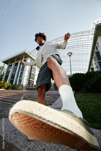Vertical shot of teenage African American boy playfully kicking camera while having fun outside in city, fisheye effect, copy space