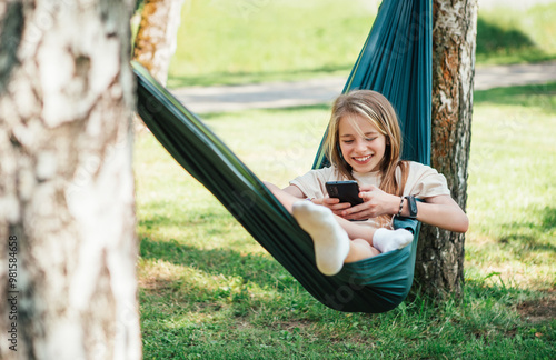 Canvas Print Little girl enjoys sunny day swinging in hammock and browsing internet using cell phone in serene forest setting