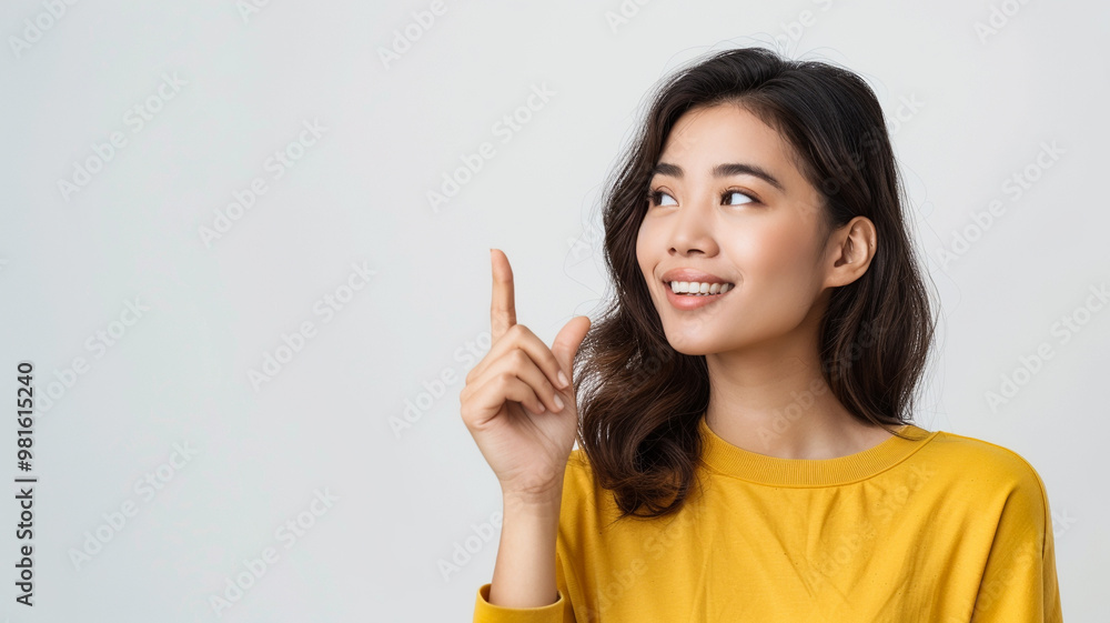 A smiling young woman with wavy dark hair wearing a yellow shirt, looking up and pointing with a cheerful, curious expression, set against a clean white background A smiling young woman with wavy dark hair wearing a yellow shirt, looking up and pointing with a cheerful, curious expression, set against a clean white background