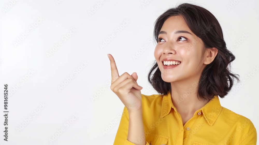 A cheerful young woman with short dark hair wearing a yellow shirt, smiling brightly and pointing upward with a joyful expression, set against a clean white background A cheerful young woman with short dark hair wearing a yellow shirt, smiling brightly and pointing upward with a joyful expression, set against a clean white background