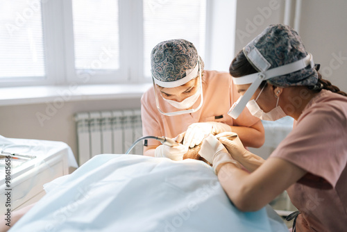 Professional two female trichologist collecting hair follicles from back of head of male patient for hair transplantation in clinic. Process of hair transplant with FUE Sapphire method. photo