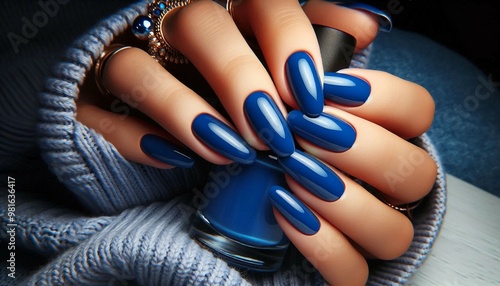 A close-up of a hand showcasing shiny blue manicured nails, with jewelry on the fingers, holding a bottle of nail polish.

 photo