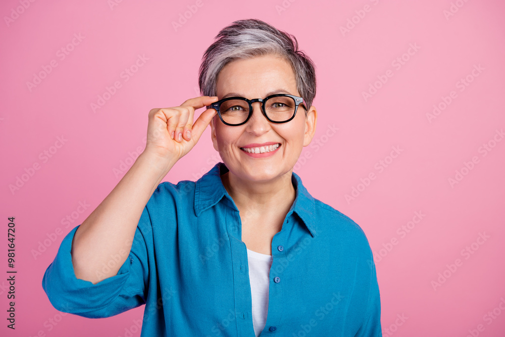 Photo portrait of pretty retired female touch eyewear smile wear trendy blue outfit isolated on pink color background Photo portrait of pretty retired female touch eyewear smile wear trendy blue outfit isolated on pink color background
