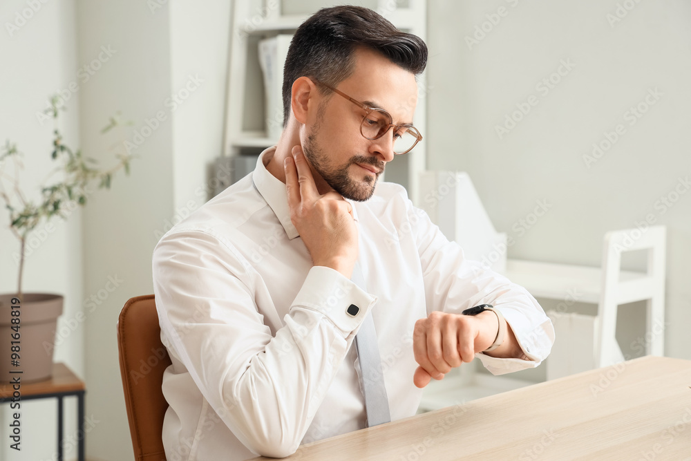 Fototapeta premium Young businessman with smartwatch checking his pulse at table in office