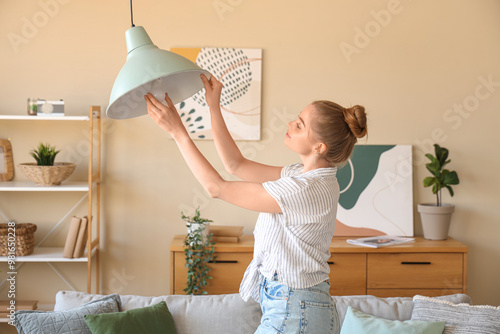 Young woman screwing light bulb into ceiling lamp at home