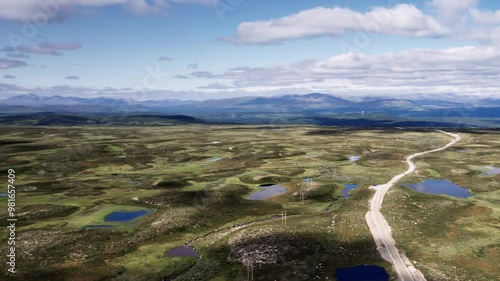 Drone flying sideways as camera zooms out, dirt road winding through the tundra landscape of the Flatruet High Fell plateau. With ponds, heathland and the mountains on the horizon in Jämtland Sweden photo