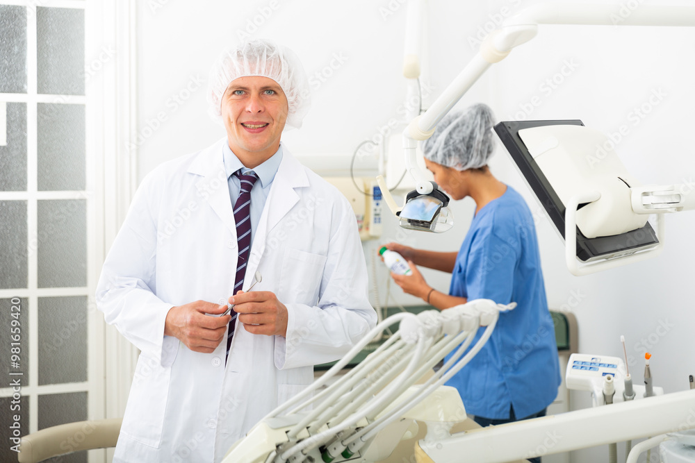 Obraz premium Positive male dentist standing in dental office looking at the camera