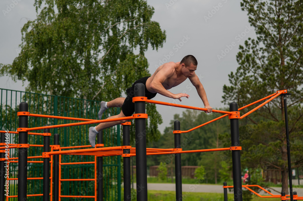 Fototapeta premium A shirtless man is doing a workout on the horizontal bars outdoors.