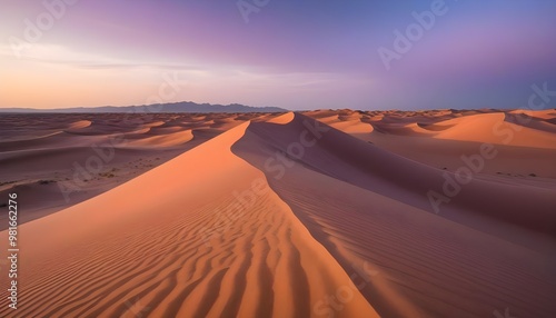 An expansive desert landscape at sunset, where the sand dunes are painted with shades of deep orange, pink, and purple.