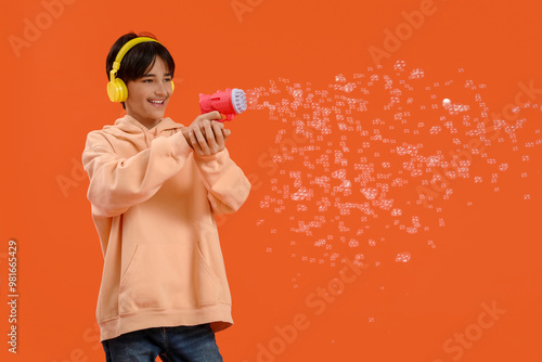 Teenage boy in headphones blowing soap bubbles on orange background