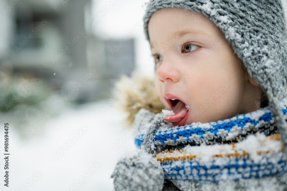 Adorable little boy having fun in a city on snowy winter day. Cute child wearing warm clothes playing in a snow. Adorable little boy having fun in a city on snowy winter day. Cute child wearing warm clothes playing in a snow.