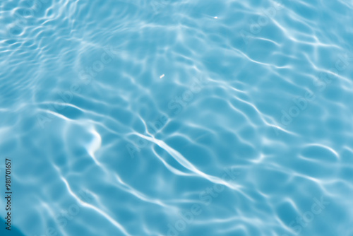 Blue water with ripples on the surface. Defocus blurred transparent blue colored clear calm water surface texture with splashes and bubbles. Water waves with shining pattern texture background.