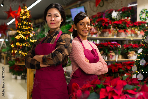 Portrait of two smiling colleagues saleswomen in work aprons posing at flower shop photo