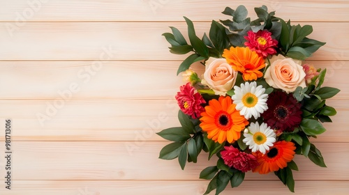 Top view of a mixed bouquet of flowers, including roses, lilies, and daisies, arranged in a circular pattern on a light wooden backgroundThe vibrant colors and natural textures create a joyful photo