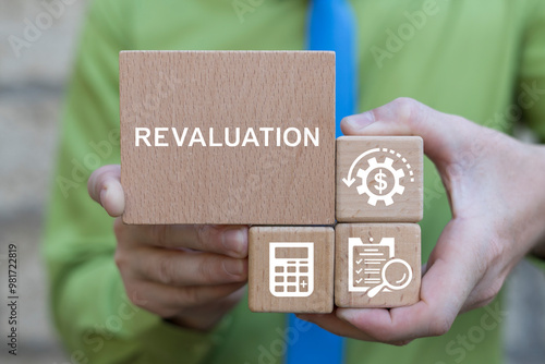 Business man holding wooden blocks with icons and text sees word: REVALUATION. Revaluation Business Failure Finance Crisis concept. Revalue and calculate.