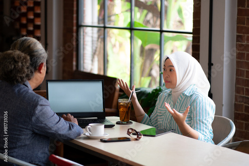 A young Asian female worker wearing a hijab presenting her work to her boss while working remotely at a cafe, the concept of remote working, working from anywhere. 