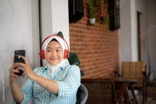 a young Asian female worker in a hijab takes a selfie in between working remotely at a cafe, the concept of remote working, working flexibly from anywhere.
 photo