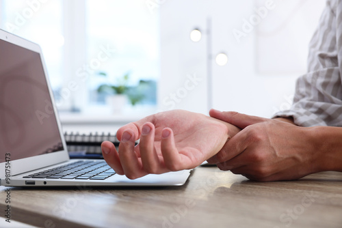 Tablou pe pânză Man suffering from pain in wrist while working on laptop at table indoors, closeup