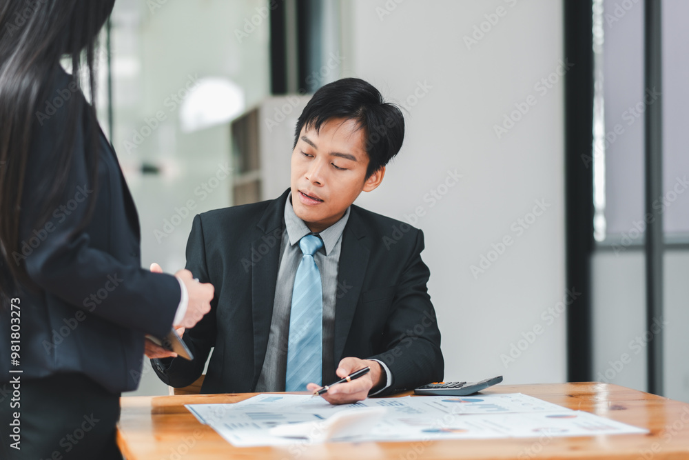 Professional Asian businessman in a suit discussing documents with a colleague in a modern office setting. Professional Asian businessman in a suit discussing documents with a colleague in a modern office setting.