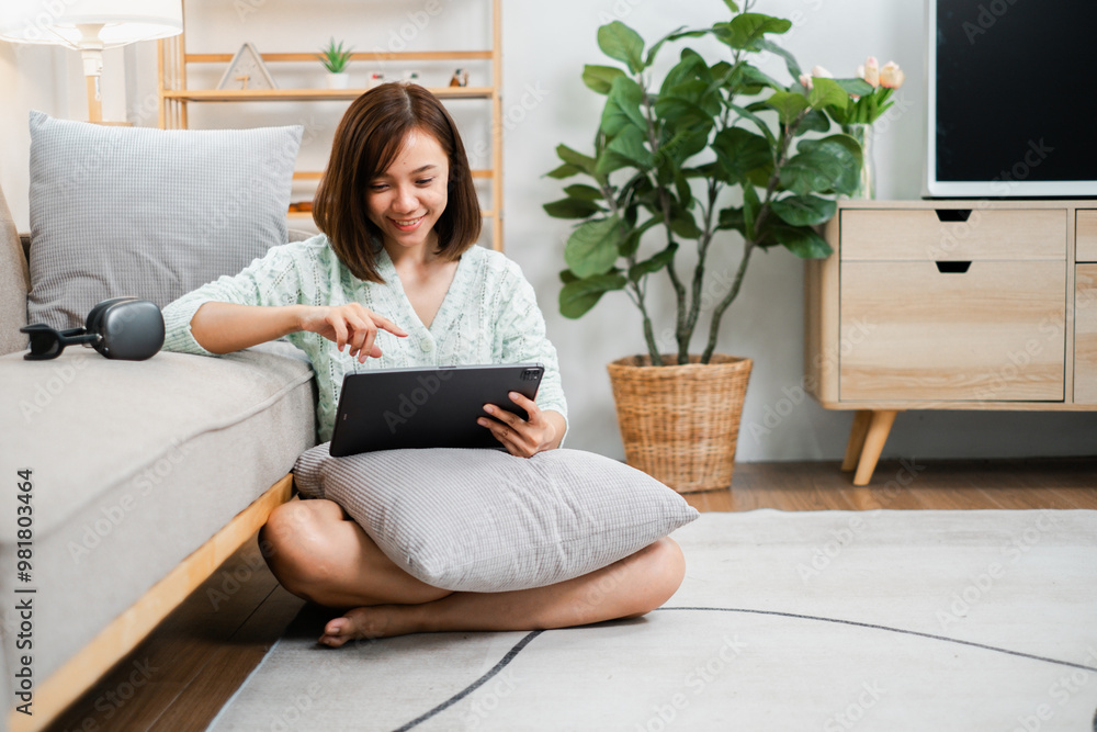 A woman sits comfortably on the floor, using a tablet in a modern living room with stylish decor and indoor plants. A woman sits comfortably on the floor, using a tablet in a modern living room with stylish decor and indoor plants.