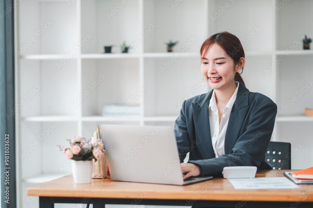 Smiling young woman in business attire working on a laptop at a desk in a contemporary office setting. Smiling young woman in business attire working on a laptop at a desk in a contemporary office setting.