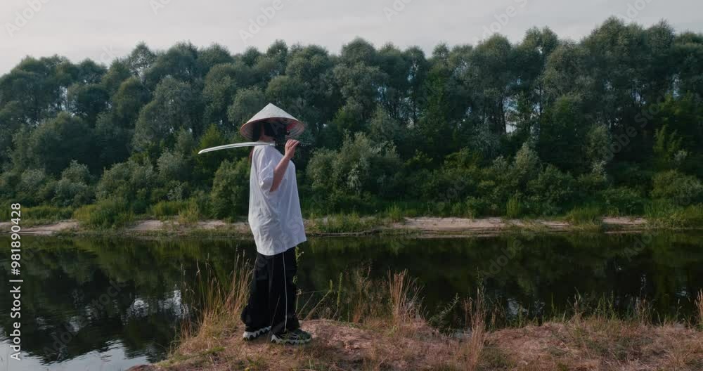 A beautiful woman on the edge of a cliff by the river with a katana in a mask and a straw hat. A samurai woman with a thoughtful look stands with a katana on a cliff and looks into the distance. A beautiful woman on the edge of a cliff by the river with a katana in a mask and a straw hat. A samurai woman with a thoughtful look stands with a katana on a cliff and looks into the distance.