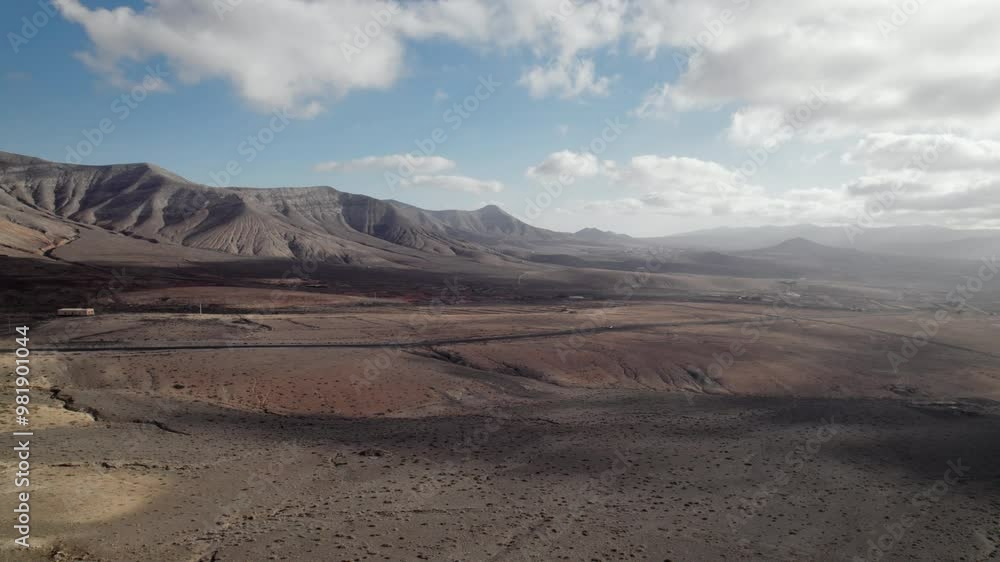 aerial shot of desert valley with mountain range on an island with desolate landscape and partly cloudy sky aerial shot of desert valley with mountain range on an island with desolate landscape and partly cloudy sky
