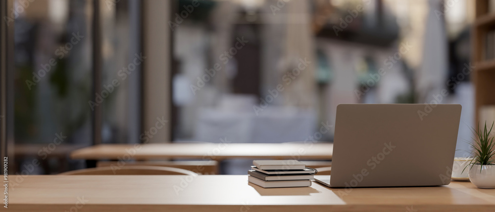 A rear view of a laptop and books on a wooden tabletop in a contemporary coffee shop.