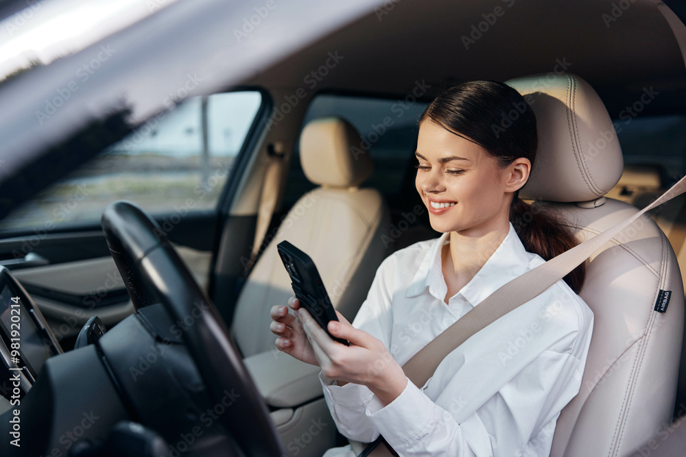 A woman in the driver's seat of her car looks at her cell phone screen, engaged in using her mobile device A woman in the driver's seat of her car looks at her cell phone screen, engaged in using her mobile device